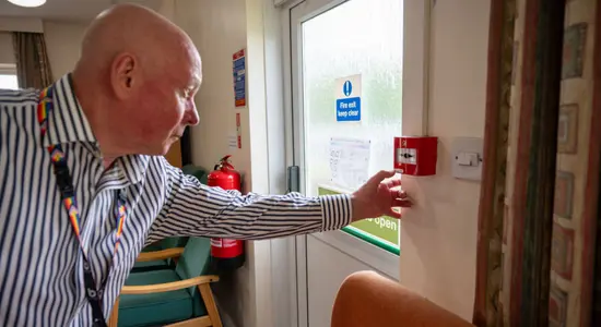 A colleague at Berneslai Homes pressing a red fire alarm.png